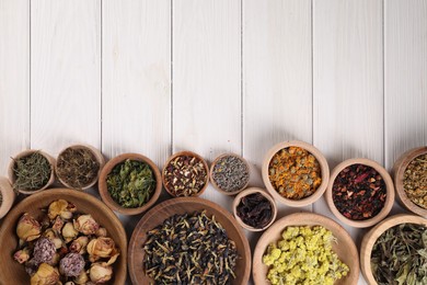 Many different dry herbs and flowers in bowls on white wooden table, flat lay. Space for text