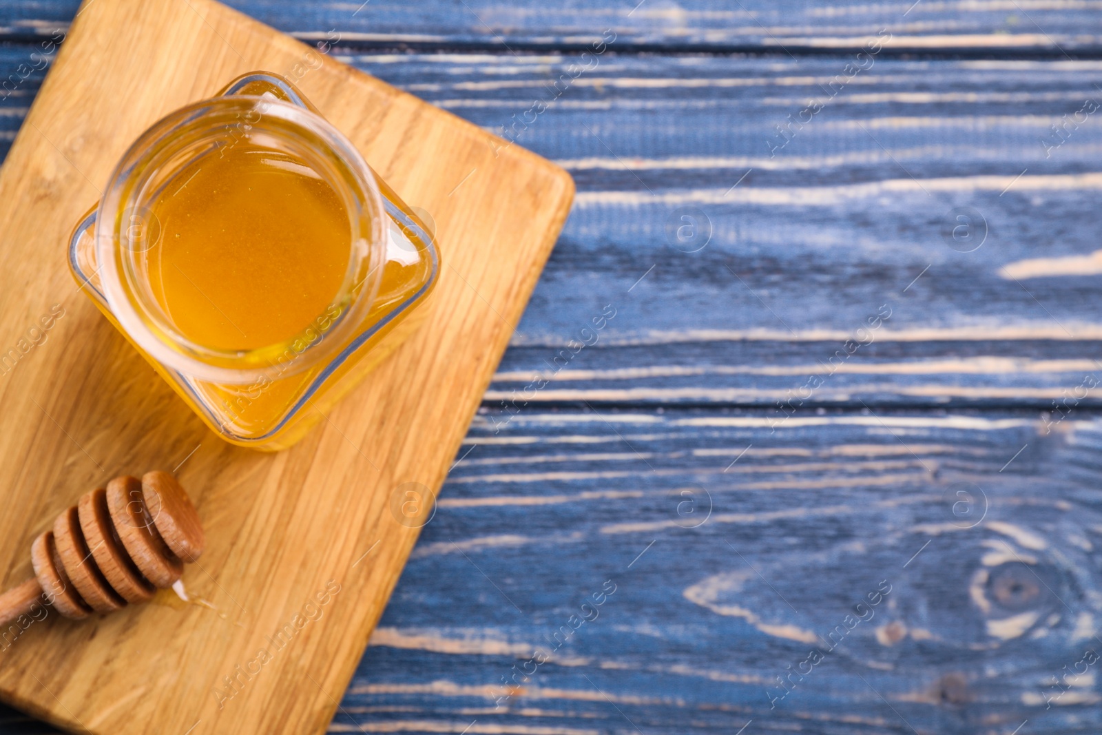 Photo of Tasty honey on blue wooden table, flat lay. Space for text