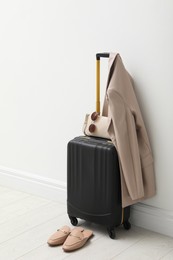 Photo of Suitcase packed for trip, shoes, jacket and accessories near white wall indoors