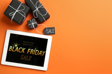 Photo of Tablet with Black Friday announcement and gifts on orange background, flat lay. Space for text