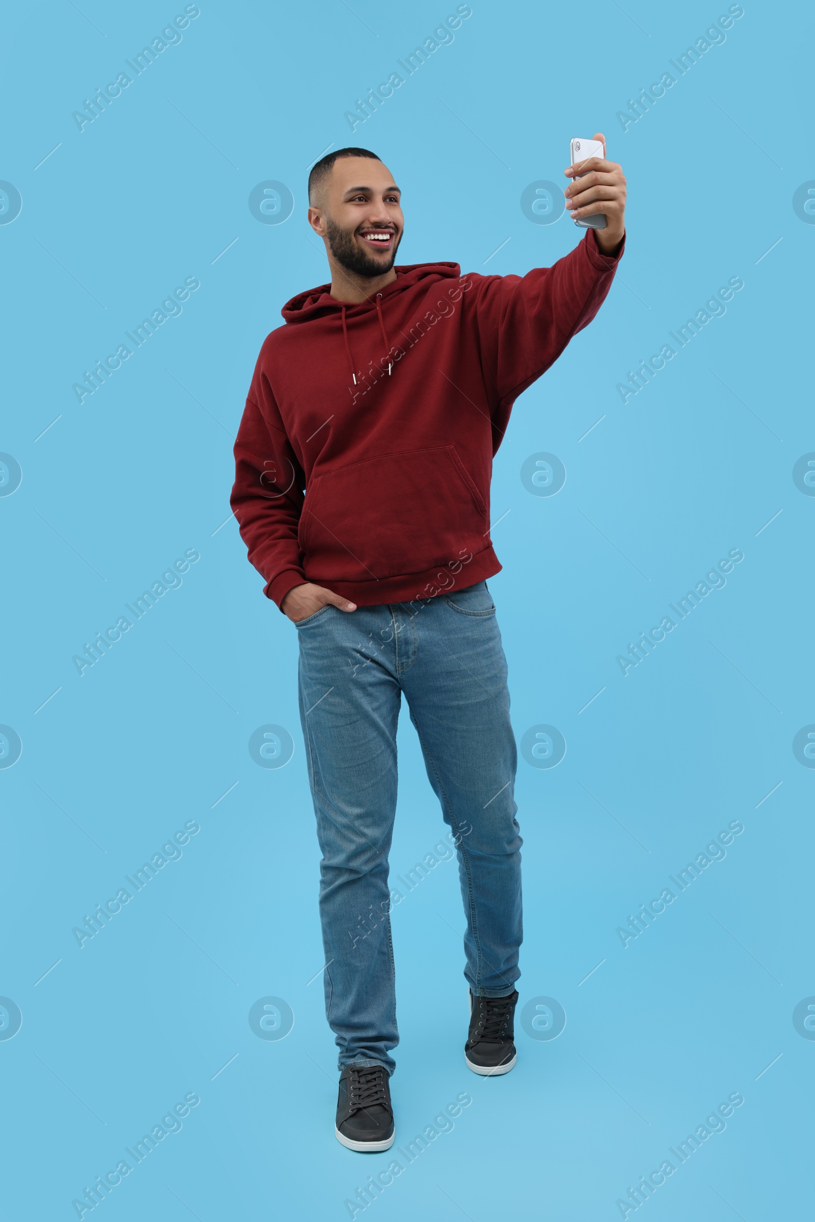 Photo of Smiling young man taking selfie with smartphone on light blue background