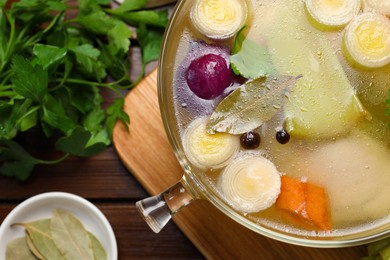 Glass pot with tasty bouillon and different ingredients on wooden table, flat lay