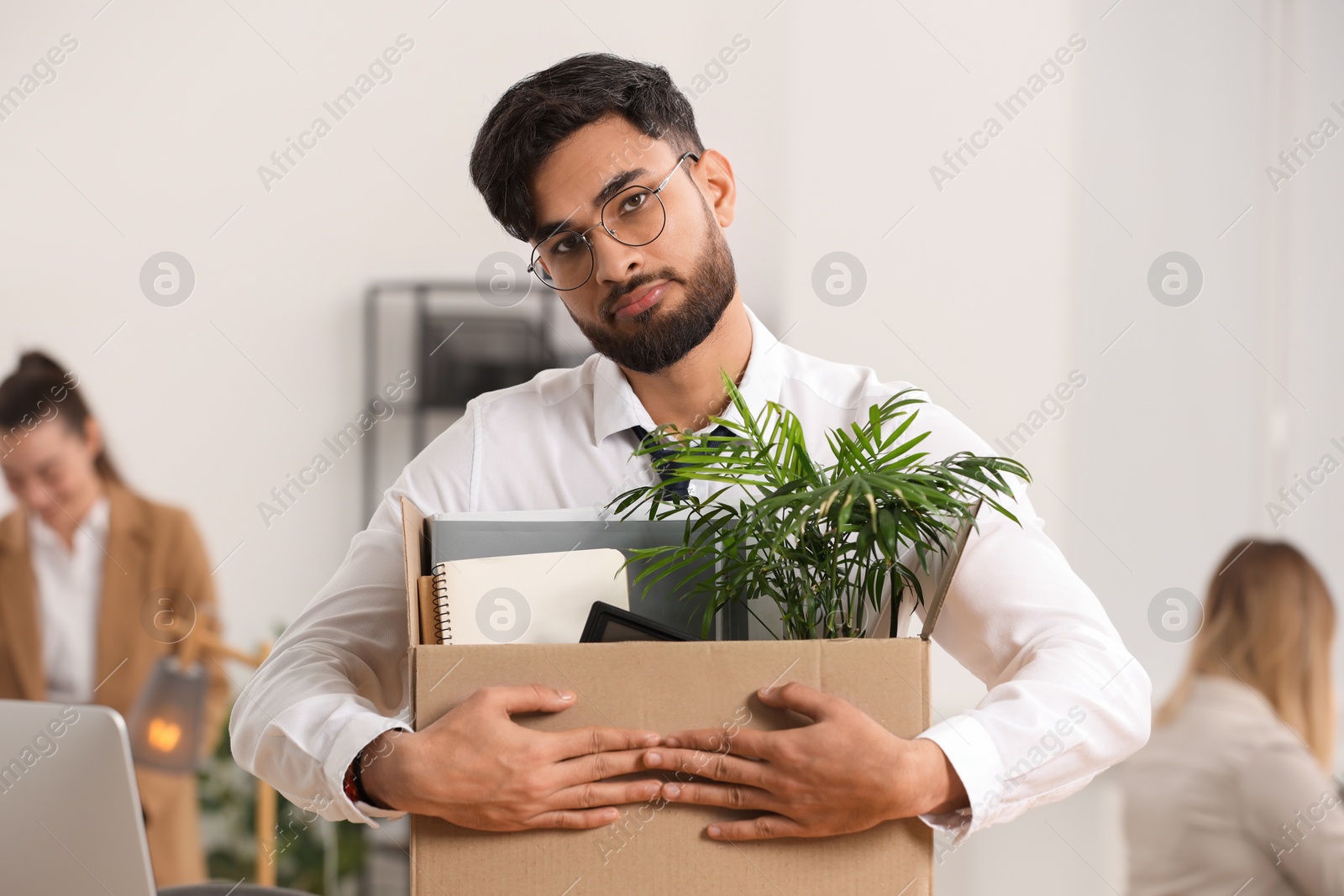 Photo of Unemployment problem. Frustrated man with box of personal belongings in office