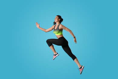 Photo of Athletic young woman running on light blue background, side view