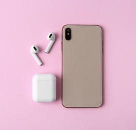 Photo of Wireless earphones, mobile phone and charging case on pink background, flat lay