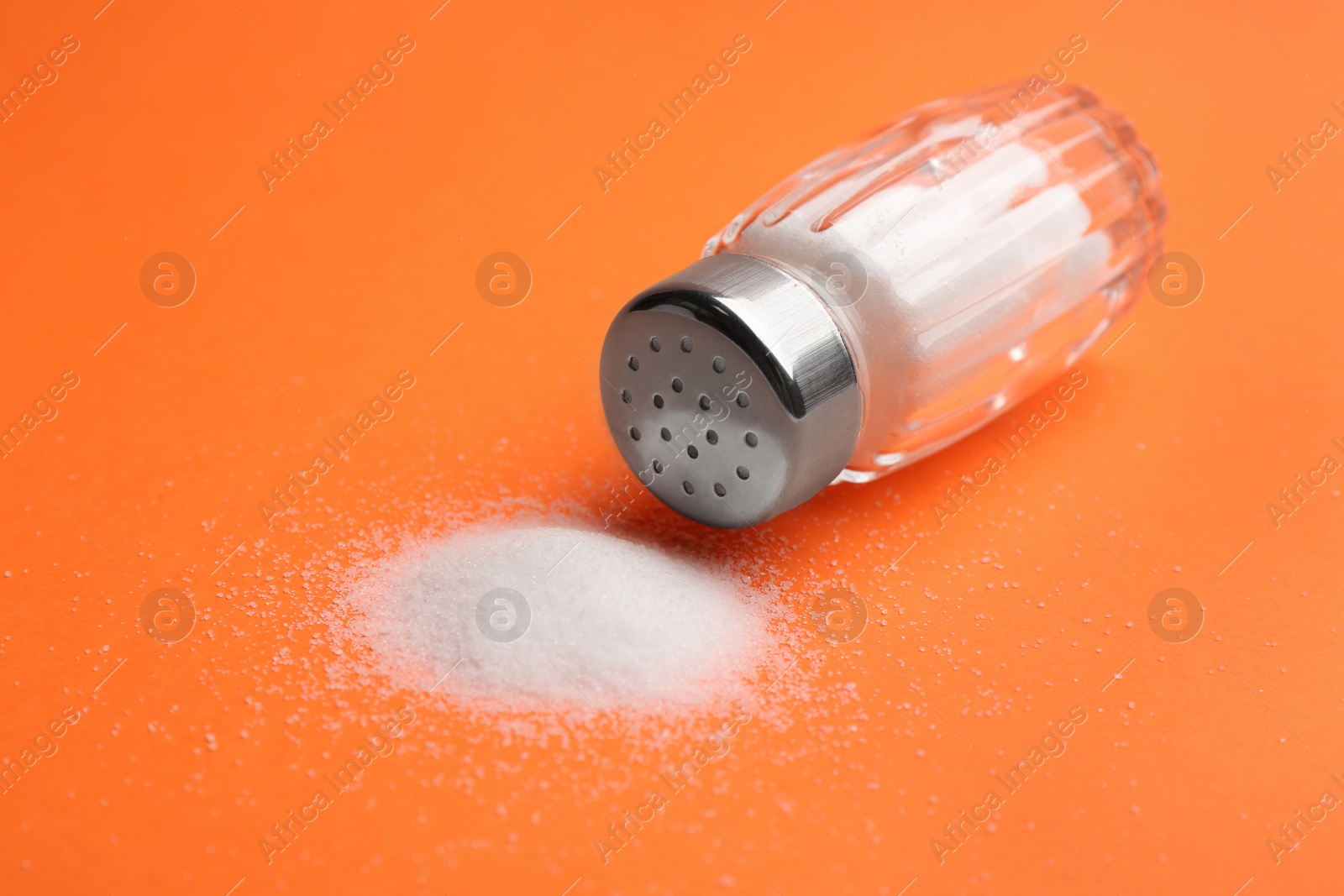 Photo of Scattered salt and shaker on orange background, closeup