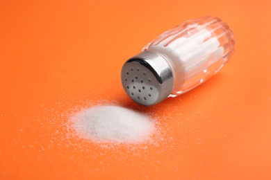 Photo of Scattered salt and shaker on orange background, closeup