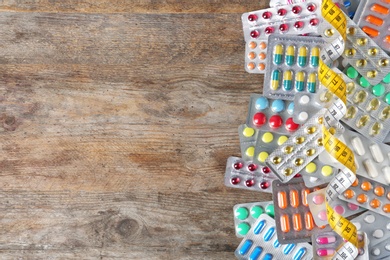 Weight loss pills in blister packs and measuring tape on wooden background, top view. Space for text