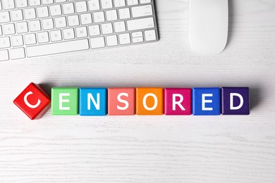 Colorful cubes with word Censored, keyboard and computer mouse on white wooden table, flat lay