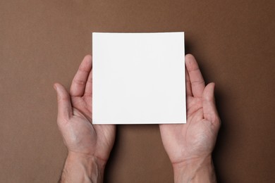 Photo of Man holding sheet of paper on brown background, top view. Mockup for design