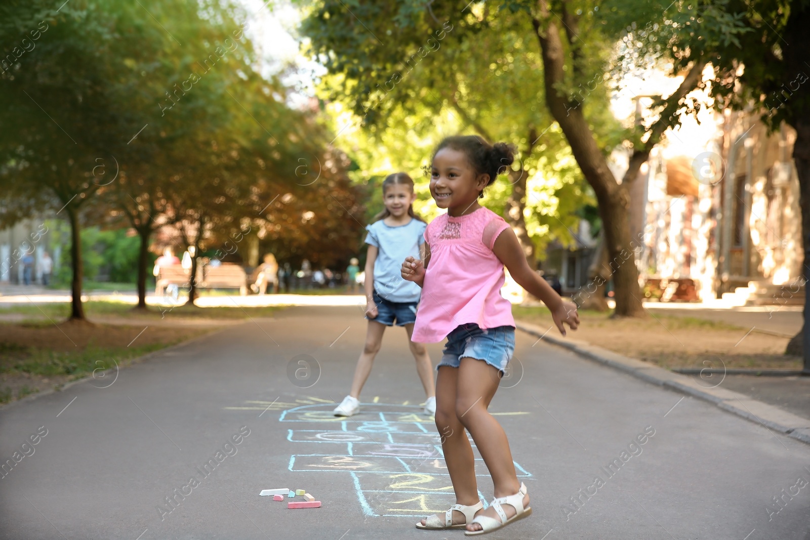 Photo of Little children playing hopscotch drawn with colorful chalk on asphalt