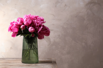 Beautiful peony bouquet in vase on wooden table against grey background. Space for text