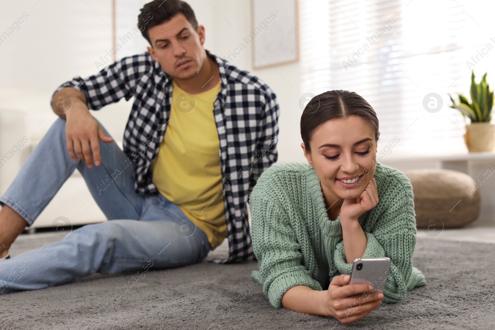 Photo of Distrustful man peering into girlfriend's smartphone at home. Jealousy in relationship