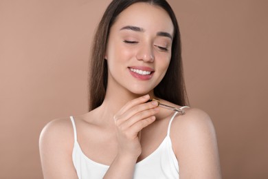 Photo of Beautiful young woman applying essential oil onto shoulder on brown background