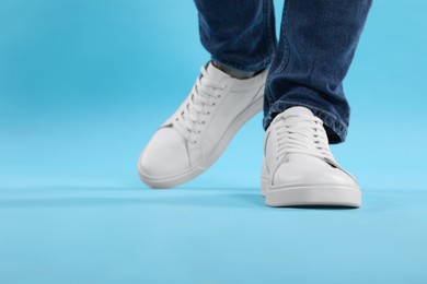 Photo of Man wearing stylish white sneakers on light blue background, closeup