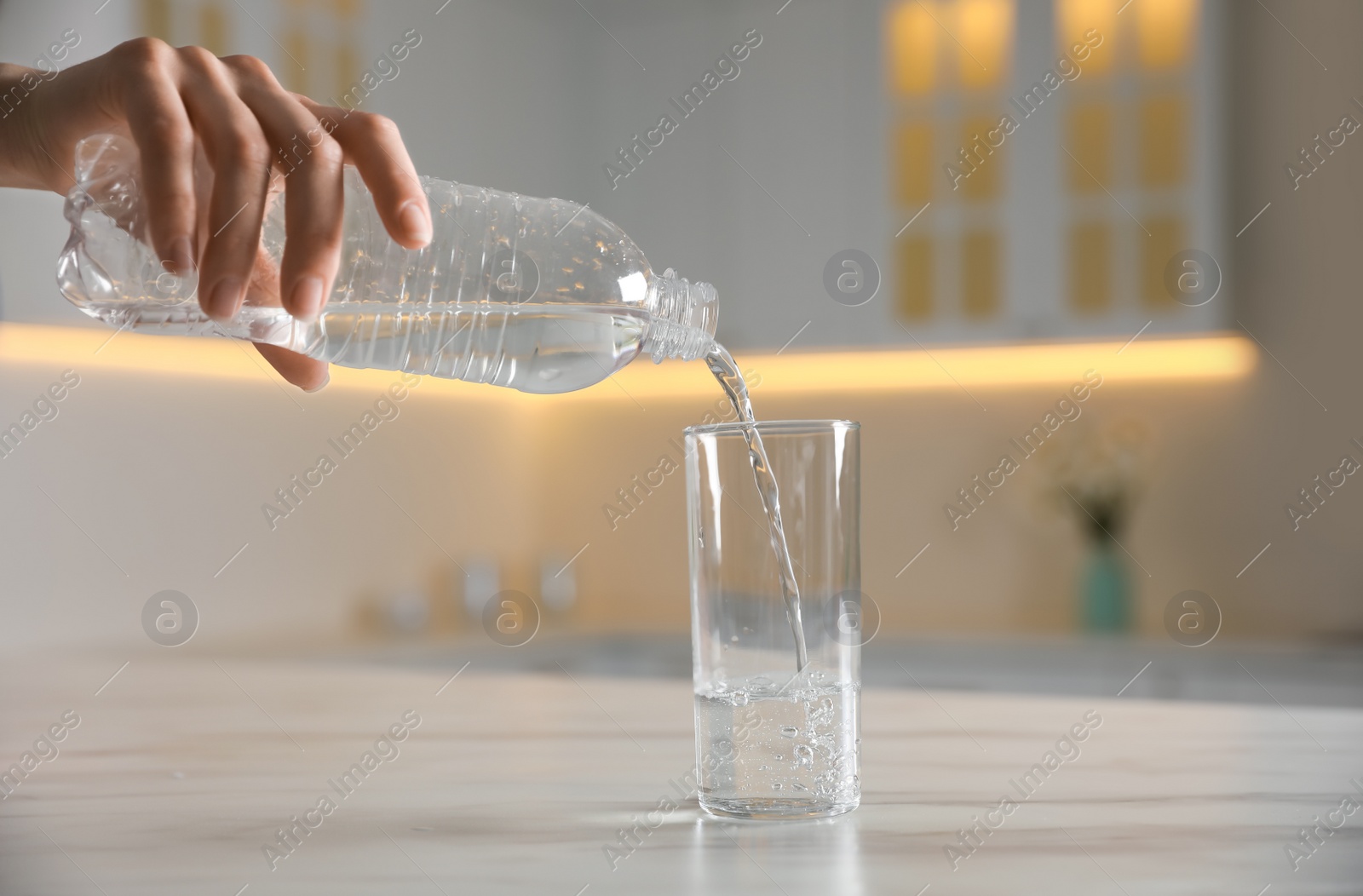 Photo of Woman pouring water from bottle into glass on table indoors, closeup