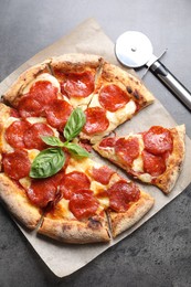 Tasty pepperoni pizza with basil and cutter on grey table, top view