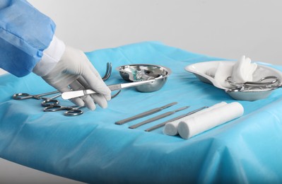 Photo of Doctor holding forceps over table with surgical instruments against light background, closeup