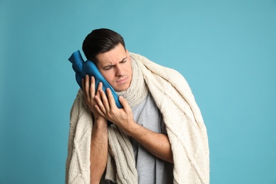Photo of Ill man with hot water bottle suffering from cold on light blue background