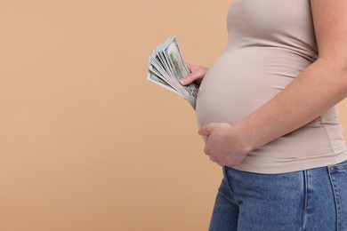 Surrogate mother. Pregnant woman with dollar banknotes on beige background, closeup. Space for text