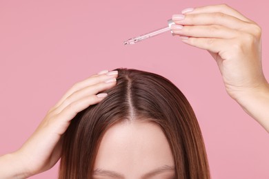 Photo of Woman applying serum onto hair on pink background, closeup