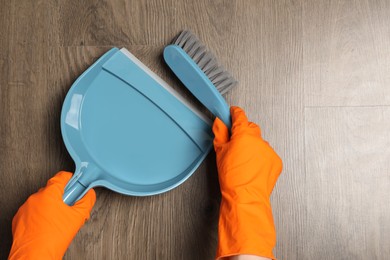Photo of Woman in gloves sweeping wooden floor with plastic whisk broom and dustpan, top view