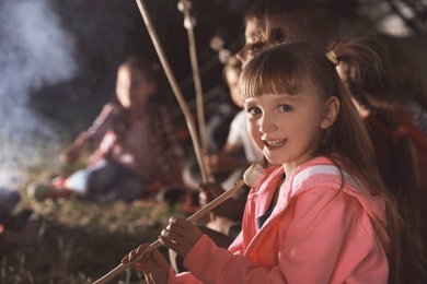 Photo of Little girl with marshmallow near bonfire at night. Summer camp
