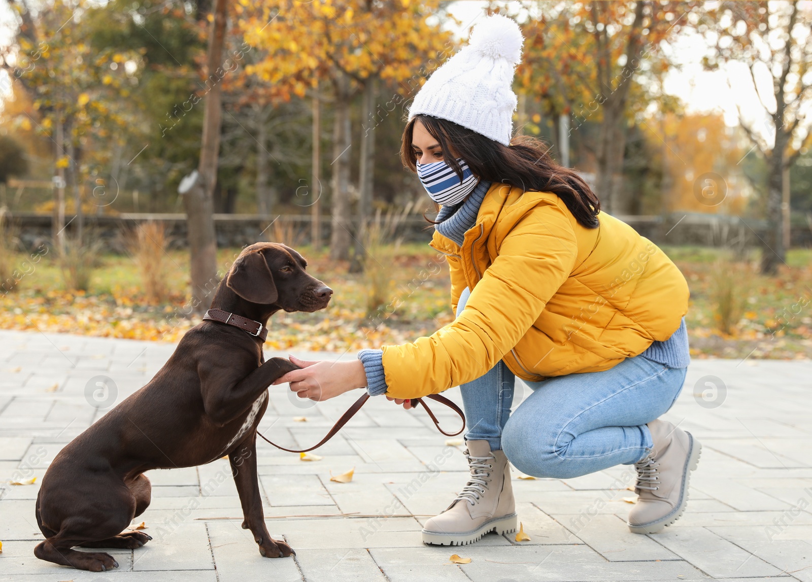 Photo of Woman in protective mask with German Shorthaired Pointer in park. Walking dog during COVID-19 pandemic