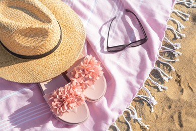 Photo of Blanket with stylish slippers, sunglasses and straw hat on sandy beach, flat lay