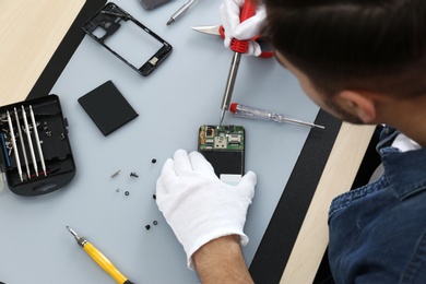 Photo of Technician repairing broken smartphone at table, closeup