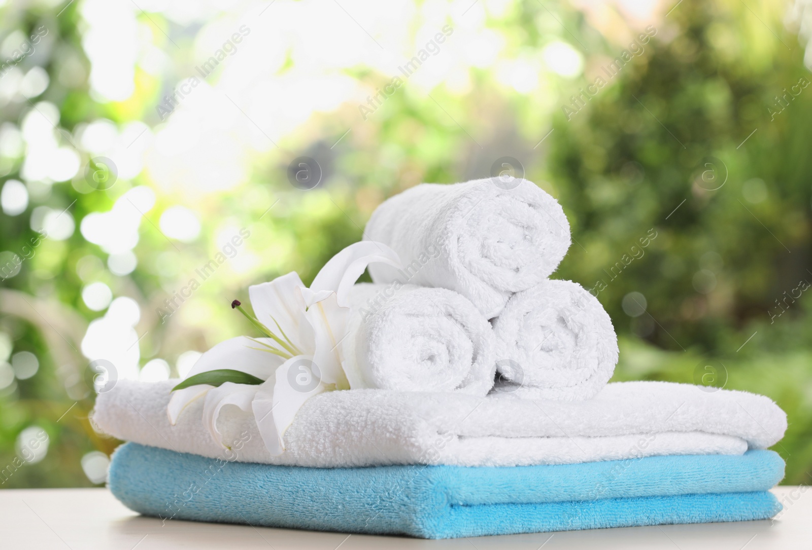 Photo of Soft bath towels and flower on table against blurred background