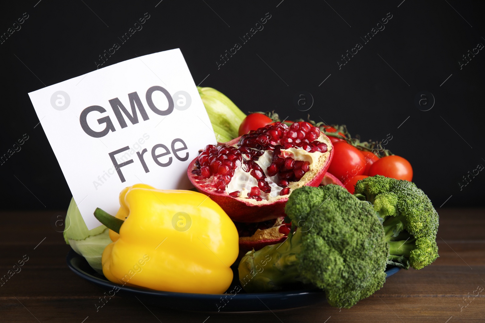 Photo of Tasty fresh GMO free products and paper card on wooden table against black background