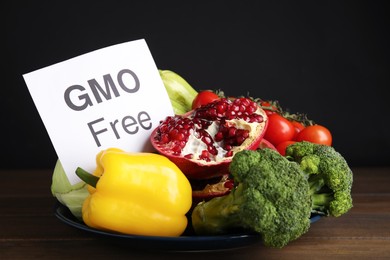 Photo of Tasty fresh GMO free products and paper card on wooden table against black background