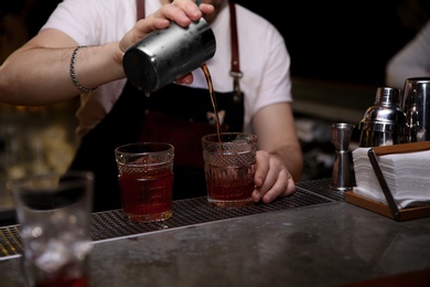 Photo of Bartender pouring tasty cocktail at counter in nightclub, closeup