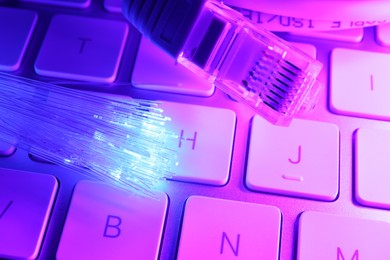 Photo of Optical fiber strands transmitting color light near cable with modular connector on computer keyboard, closeup