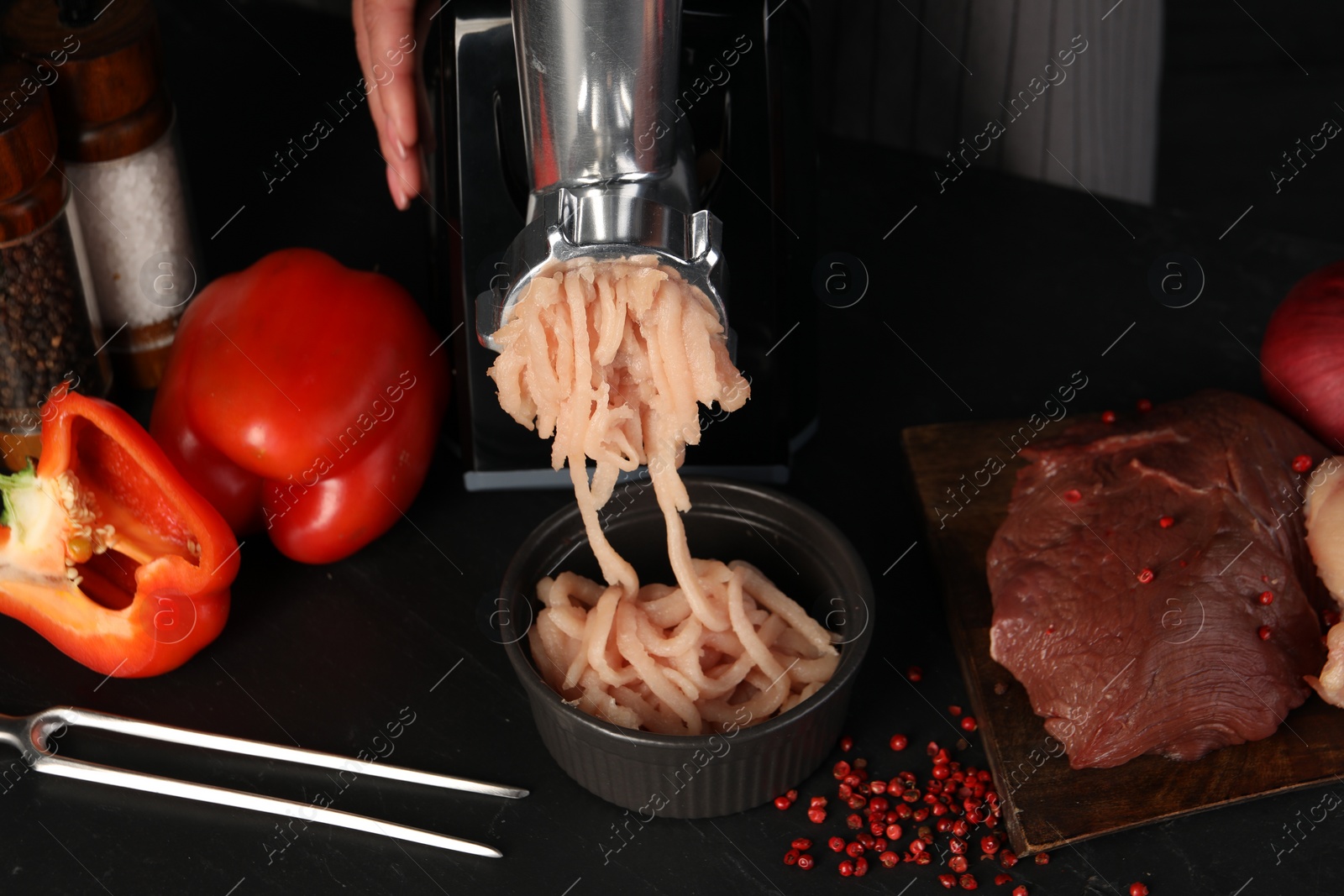 Photo of Woman making chicken mince with electric meat grinder at black table, closeup