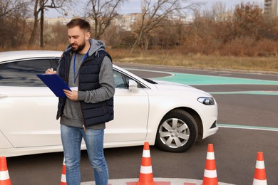 Photo of Instructor with clipboard near car outdoors. Driving school exam