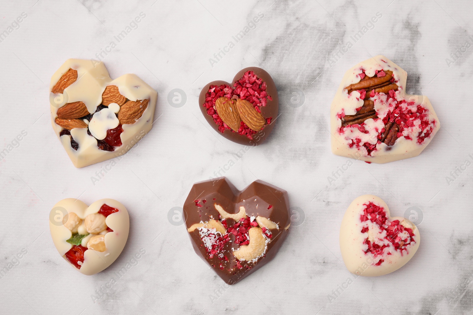 Photo of Tasty chocolate heart shaped candies with nuts on white marble table, flat lay