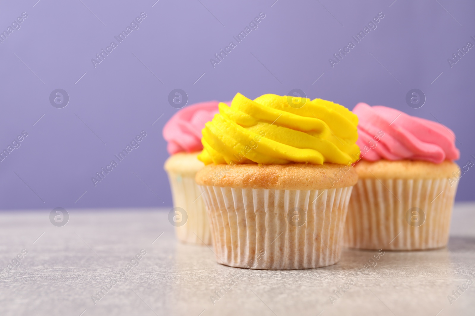 Photo of Delicious cupcakes with bright cream on gray table against violet background, space for text