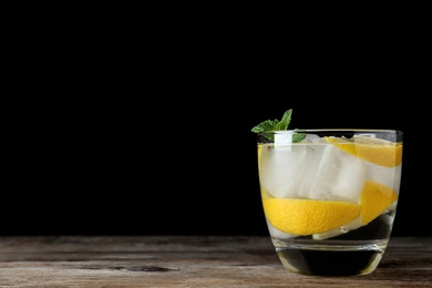 Vodka cocktail with lemon and ice on wooden table against black background. Space for text