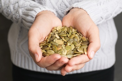 Photo of Woman holding raw pumpkin seeds, closeup view