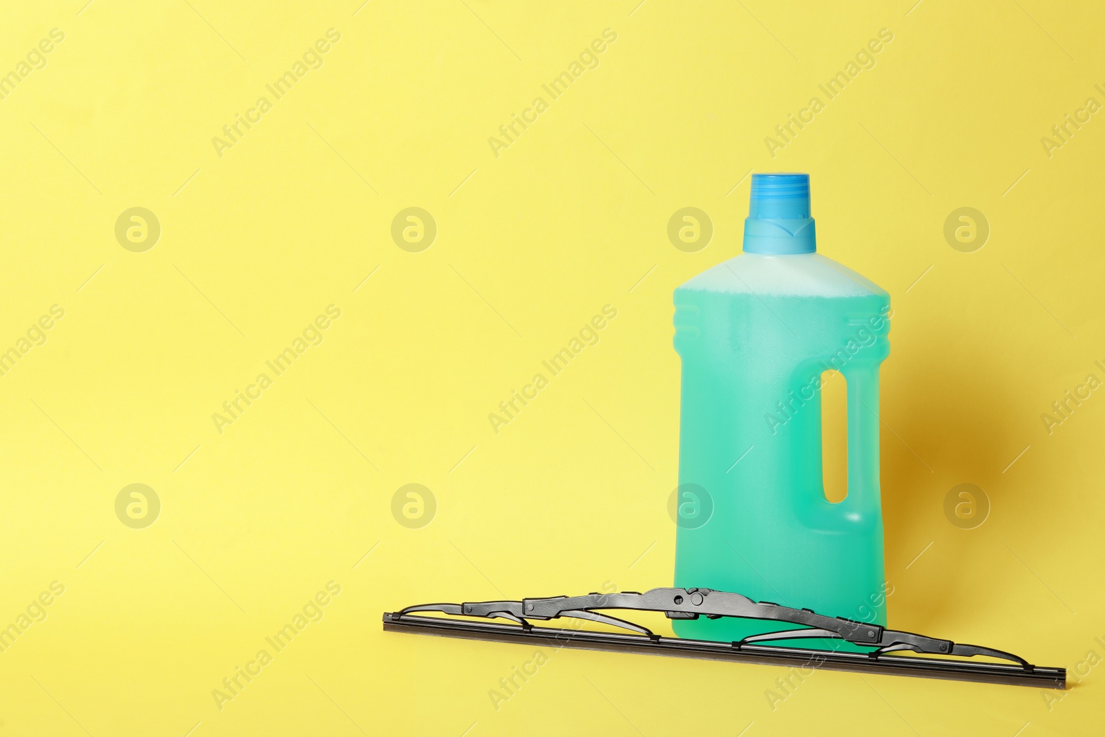 Photo of Bottle of windshield washer fluid and wiper on yellow background. Space for text