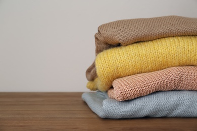 Stack of knitted sweaters on wooden table. Space for text