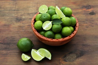 Photo of Whole and cut fresh ripe limes in bowl on wooden table