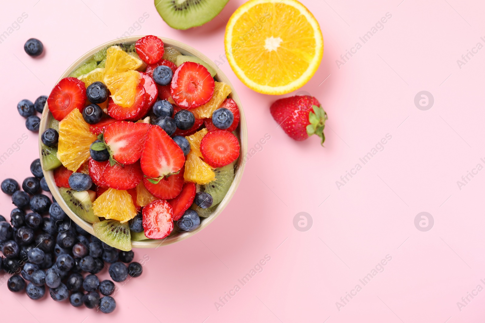 Photo of Yummy fruit salad in bowl and ingredients on pink background, flat lay. Space for text
