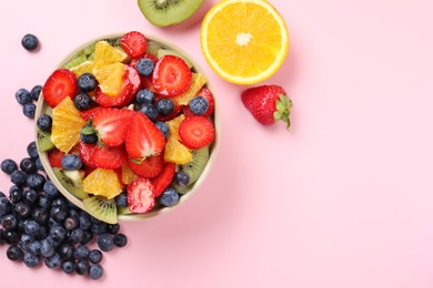 Yummy fruit salad in bowl and ingredients on pink background, flat lay. Space for text