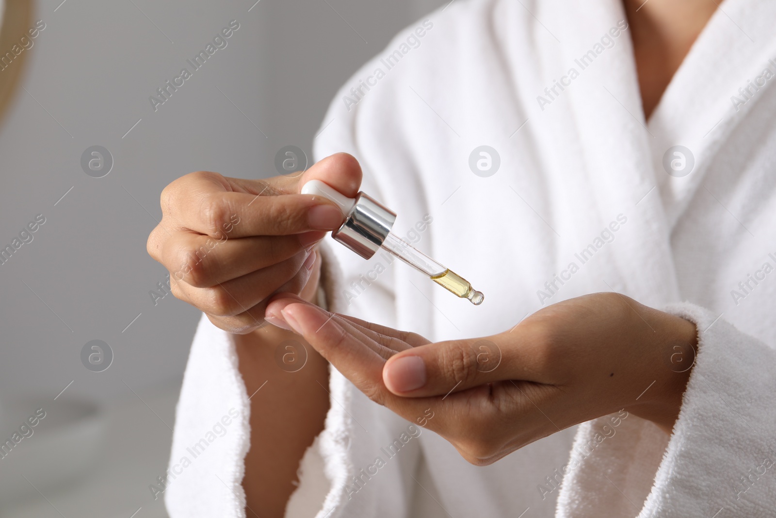 Photo of Woman applying cosmetic serum onto her hand on grey background, closeup