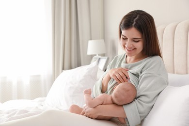 Photo of Young woman breastfeeding her little baby on bed at home