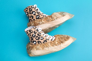 Photo of Sneakers in shoe covers on light blue background, top view