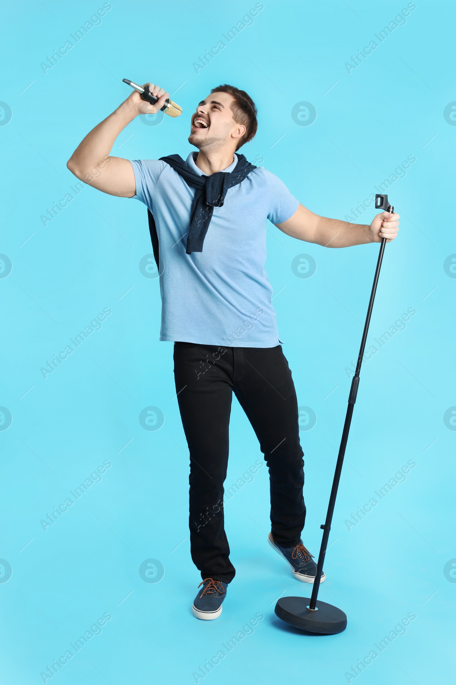 Photo of Young handsome man in casual clothes singing with microphone on color background